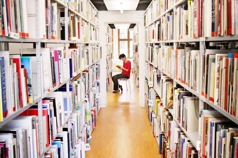 lesende Frau sitzt zwischen zwei deckenhohen Bücherregalen