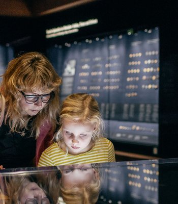 drei Besucher, darunter zwei Kinder, schauen sich Vitrine mit Münzen an
